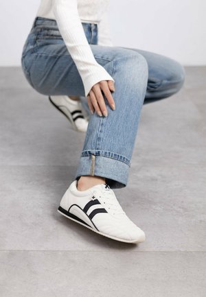 Zapatillas blancas con acentos y rayas negras, hechas de un material texturizado. Punta redondeada y suela plana con un sutil detalle de costura.