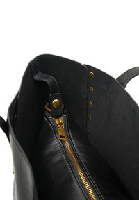 Black leather tote bag interior showing a gold zipper, black fabric lining, and brass snap buttons. Sleek design with stitching details.