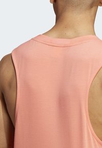 Top senza maniche di colore pesca, con scollatura rotonda e fori per le braccia arrotondati. Realizzato in tessuto liscio con una consistenza morbida.