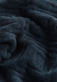 Marinblå texturerat handduksmaterial med upphöjt diamantmönster, mjuk och plyschig yta, som visar en djup, rik färg och intrikata detaljer.