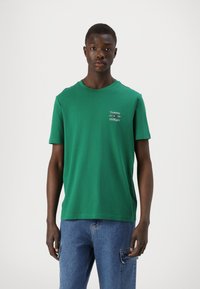 Zöld, rövid ujjú pamut póló, kerek nyakkivágással és fehér "Tommy Hilfiger" logóval. Simma textúra, laza illeszkedés.
