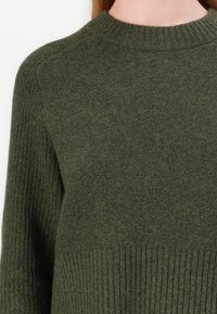 Maglione verde oliva realizzato in tessuto lavorato a maglia, con orlo a coste e scollatura rotonda, progettato con maniche lunghe e una vestibilità comoda.