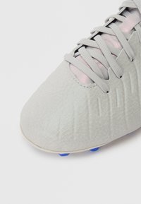 Close-up of grey leather soccer cleat with textured detailing, grey laces, pink tongue, and blue studs visible beneath the sole.