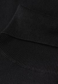 Primo piano del tessuto di un maglione nero a maglia, con una texture a coste e dettagli di polsini spessi. Il materiale appare morbido ed elastico.