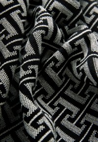 Țesătură alb-negru cu o textură împletită, având un model geometric de forme interconectate. Apariție moale, drapată.