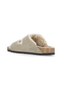Sandal in suede beige senza chiusura, con fodera in shearling, sottopiede in sughero e suola in gomma nera texturizzata. Presenta due aperture a taglio sulla tomaia.