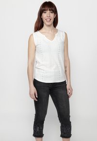 Valge sansleeve top V-kaelusega, millel on augulised mustrid. Sobitatud tumedate denimpükste vahel pükstes, mille hem on kaunistatud detailse tikandiga.