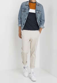 Jeansová bunda, tričko s barevným blokem v námořnické modré a oranžové barvě, světle béžové zúžené kalhoty a bílé tenisky s texturovanou podrážkou a kotníkovými ponožkami.