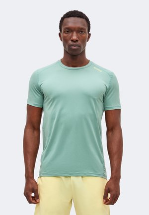 Άνδρας που φοράει εφαρμοστό κοντομάνικο πουκάμισο μέντας με το λογότυπο "BORG" στον ώμο και ανοιχτό κίτρινο σορτς, στέκεται με το πρόσωπο προς τα εμπρός.