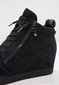 Baskets compensées en cuir suédé bleu foncé, avec un motif texturé, une fermeture éclair sur le côté et des accents cloutés. Semelle en caoutchouc noire et design à lacets.