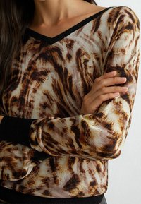 Maglione a V in un tessuto leggero e trasparente con motivi astratti marroni e crema. Presenta polsini e orlo a coste neri.