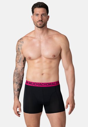 Melni bokseri ar rozā elastīgu jostu, uz kuras ir redzams zīmola nosaukums "MUCHACHOMALO." Gluda tekstūra, pieguļošs dizains un vidējais garums līdz augšstilbam.