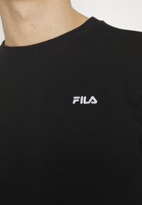 T-shirt in cotone nero con colletto girocollo a costine e logo "FILA" ricamato in bianco sul petto, caratterizzato da una texture liscia.
