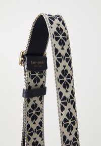 Sangle ajustable Kare Spade avec un motif floral noir sur fond crème, avec une section en tissu bleu marine et des accents en métal doré.
