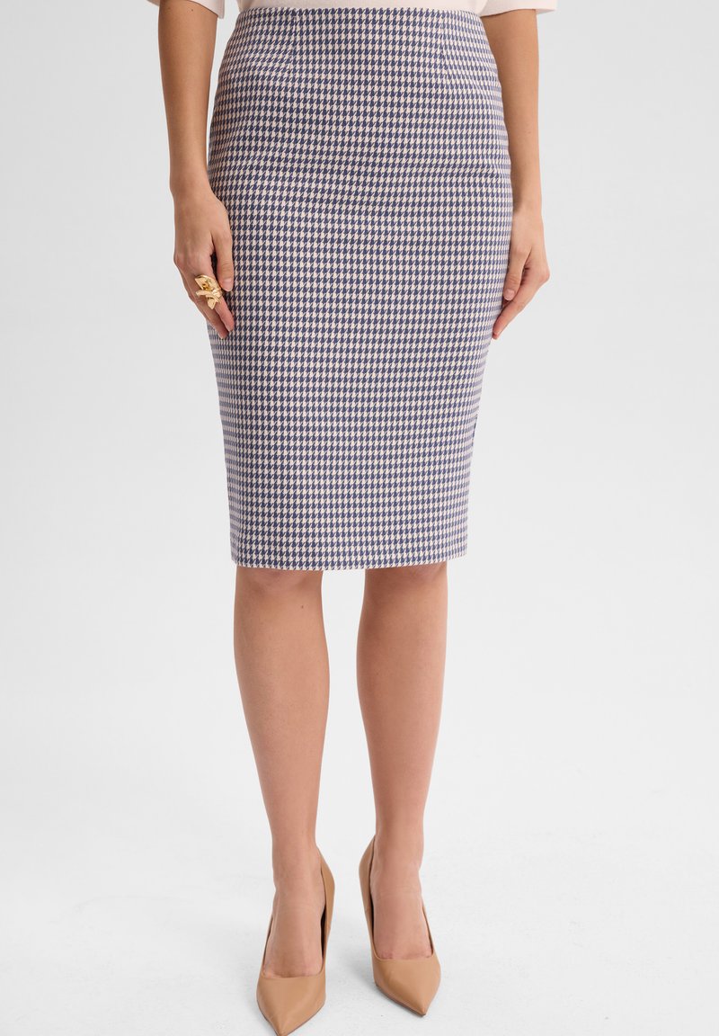 Spódnica o długości do kolan w kształcie ołówka, w granatowo-białą kratę houndstooth, wykonana z wytrzymałego materiału. Noszona z cielistymi szpilkami.