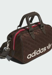 Brown patterned duffle bag with red zipper, dual top handles, and removable shoulder strap. Features white Adidas logo on side.