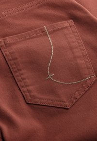 Roestkleurige stof met een zak voorzien van groene contrasterende stiksels en een decoratief ontwerp-element. Soepele textuur, op maat gemaakte zakvorm.