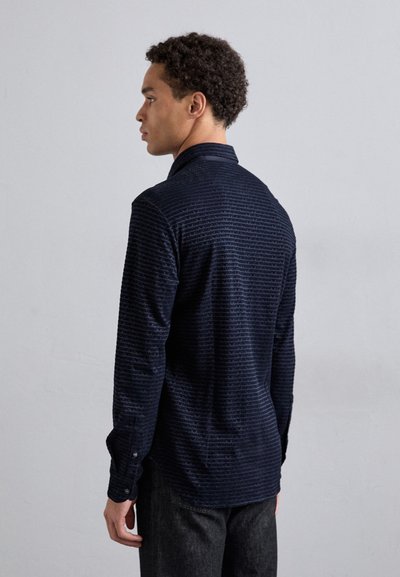 Camicia blu navy con righe orizzontali testurizzate, caratterizzata da un colletto a punta e maniche lunghe, mostrata con una vista dal retro.