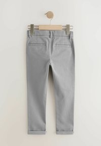 Pantalons en mélange de coton gris avec une coupe slim, dotés de deux poches arrière, d'un ourlet roulé, et accrochés sur un cintre en bois.