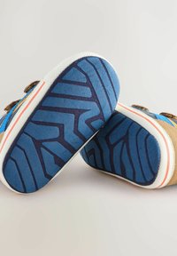 Baskets bleues et beige avec une semelle en caoutchouc texturé présentant un motif de grip en zigzag. L'intérieur de couleur claire et des accents marron sont visibles.
