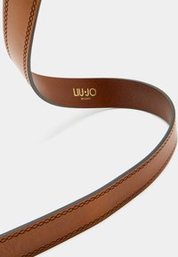 Cintura marrone in ecopelle con cuciture in rilievo e una leggera lucentezza. Presenta un logo dorato "LIU.JO MILANO". Texture liscia e forma arrotondata.
