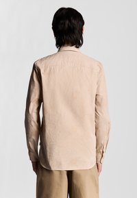 Långärmad skjorta i ljus beige med blommönster, tillverkad av mjukt tyg. Har en knapp-ner krage och manschetter med synlig sömnad.