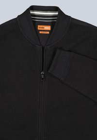 Black slim-fit bomber jacket with a textured fabric, ribbed collar, and a contrasting inner stripe. Features a zipper front closure.
