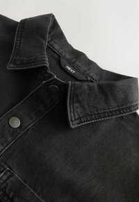 Melnas denima krekls ar klasisku apkakli, pogu akcentiem un redzamām šuvju detaļām. Mīksta tekstūra ar ikdienišķu dizainu.