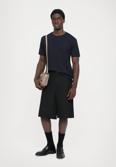 Marine crew-neck t-skjorte, svarte knelange shorts, svarte loafer-sko, svarte sokker og en lysebrun crossover-veske. Enkelfarget stoff med et avslappet design.