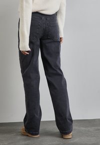 Vaqueros de lavado oscuro con un diseño de pierna recta, que cuentan con bolsillos traseros y una textura suave, combinados con un suéter crema y calzado beige.