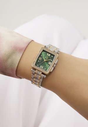 Zlata in srebrna pravokotna ura z zelenim obrazom, rimskimi številkami, diamanti ter dvobarvnim kovinskim zapestjem.