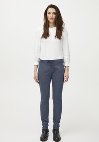 Pantalones jogger de un azul marino oscuro con cintura ajustable, junto con una camiseta blanca de manga larga con textura y botas negras hasta el tobillo.
