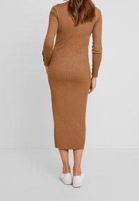 Abito midi a coste marrone con maniche lunghe, silhouette aderente e orlo dritto; indossato con sneaker bianche.