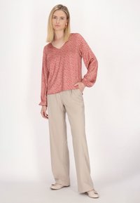 Letvægtig bluse med rosa blomsterpræget, V-hals og lange ærmer, parret med beige bredbenede bukser og lyse sko.