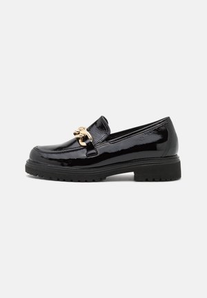 Sort laklæder loafer med tyk kraftig sål og guldkæde detalje tværs over fronten, vist i sideprofil på hvid baggrund.