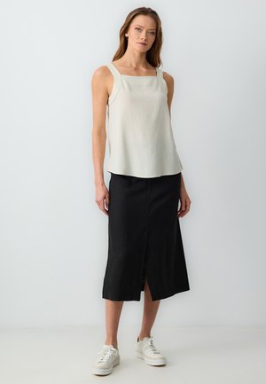 Witte mouwloze top met vierkante halslijn, gecombineerd met een lange zwarte rok met een voorwaartse split, aangevuld met witte sneakers.