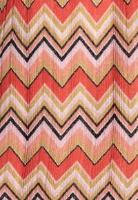 Tessuto con motivo a chevron in arancione, rosa, oro e nero. Il tessuto ha un aspetto testurizzato con una finitura leggermente lucida.