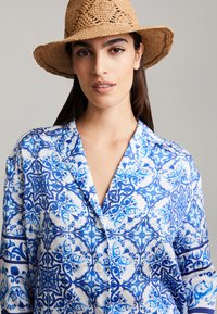 Blauw en wit gestreept shirt met een kraag, met bloem- en geometrische ontwerpen, vervaardigd van lichte stof; knoopsluiting zichtbaar.