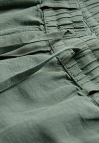 Tissu en lin vert avec une texture plissée et des liens, mettant en valeur un matériau doux et léger dans une teinte naturelle et atténuée.