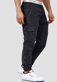 Pantalons cargo noirs avec une taille élastique et des poches latérales, présentant un tissu texturé et des jambes fuselées, associés à des baskets blanches.
