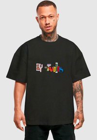 Sort t-shirt med løstsiddende pasform, prydet med multicoloreret tekst i forskellige skrifttyper, som læser "2Y Studios." lavet af bomuldsstof med korte ærmer.