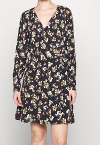 Czarna sukienka kopertowa w kwiatowy wzór w kolorach zielonym, brzoskwiniowym i białym. Posiada długie rękawy i głęboki dekolt w serek. Wykonana z lekkiego materiału.