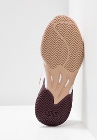 Tennarin pohja, jossa on aaltoileva rakenne vaaleanruskeassa ja tummanvioletissa, korotettu Puma-logo ja aukot joustavuuden lisäämiseksi.