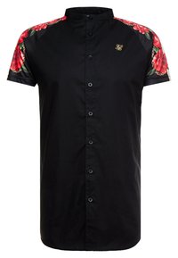 Camisa negra de manga corta con acentos florales en los hombros. Cuenta con un cierre frontal de botones y un cuello mao. Detalle del logo en dorado.