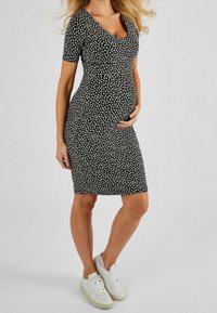 Svart gravidklänning med korta ärmar, med ett vitt blommönster. Stylad med vita sneakers, figurnära design och rundad halsringning.