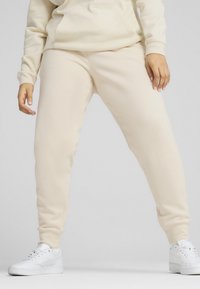Beige joggerbroek van zachte stof met een taps toelopende pasvorm, voorzien van een elastische tailleband, zijzakken en gecombineerd met witte sneakers.