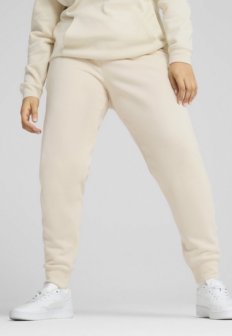Beige joggerbroek van zachte stof met een taps toelopende pasvorm, voorzien van een elastische tailleband, zijzakken en gecombineerd met witte sneakers.