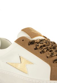 Witte leren sneaker met bruine suède details, gouden metallic accenten en gemusterde bruine veters. Bevat een opvallend gouden bliksemschichtontwerp.