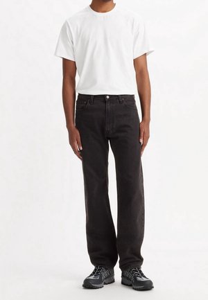 Pantalones de mezclilla negros con un ajuste de pierna recta, combinados con una camiseta blanca de manga corta sencilla y zapatillas deportivas negras. Detalles de costura mínimos.