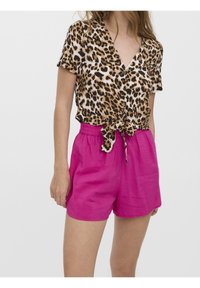 Blusa a maniche corte con stampa leopardata e davanti legato, abbinata a pantaloni corti rosa ben slacciati. Il tessuto sembra leggero con una finitura texturizzata.